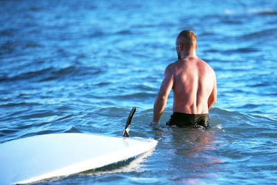 Shirtless muscular young man with surfboard in sea