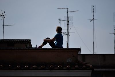 Man sitting on roof against sky