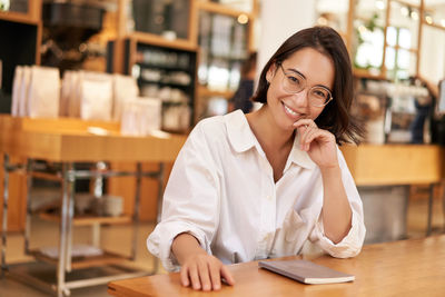 Portrait of young woman using mobile phone while sitting in cafe