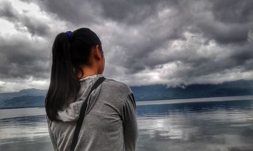 Rear view of woman at beach against cloudy sky