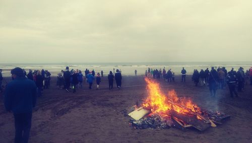 Bonfire amidst people on beach against sky