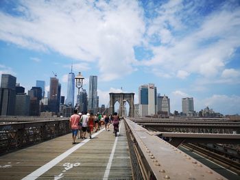 People walking on bridge against buildings in city