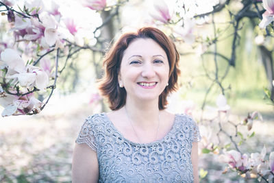 Cheerful middle aged armenian woman in an elegant dress under the magnolia blooming tree. spring pa