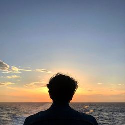 Rear view of man on sea against sky during sunset