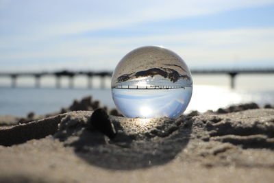 Close-up of crystal ball on beach against sky