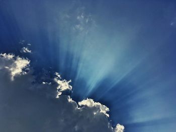 Low angle view of sunlight streaming through clouds