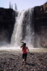 Full length of woman running towards waterfall
