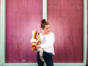 Woman carrying baby while standing against wall