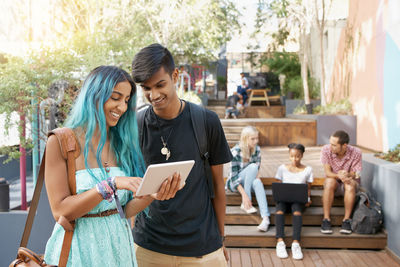 Portrait of smiling friends using digital tablet while sitting on table