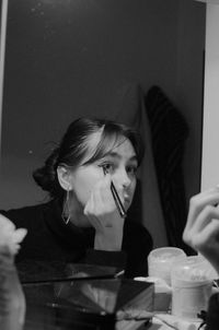 Young woman applying make-up in front of mirror