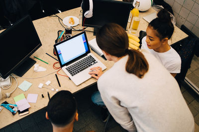 High angle view of businesswoman using laptop while standing amidst colleagues at creative office