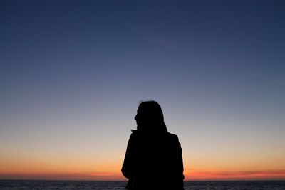 Silhouette woman standing on shore against sky during sunset