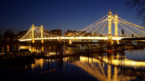 Illuminated bridge over river against sky at night