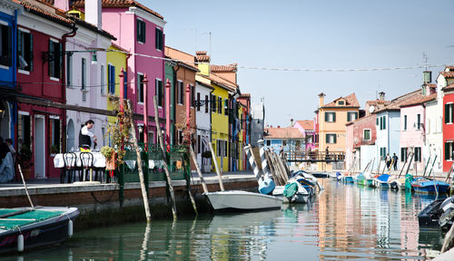 Boats moored in canal by city buildings against sky