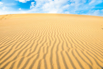 Landscape of desert sand dunes and blue sky with clouds over them