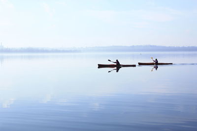 People rowing boat in lake against sky