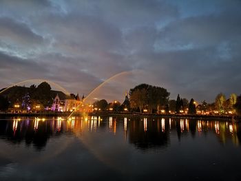Illuminated city by river against sky at dusk