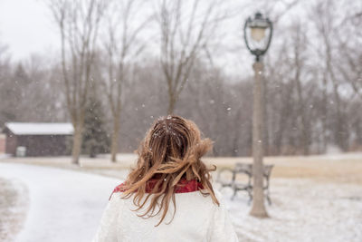 Rear view of woman standing against bare trees during snowfall