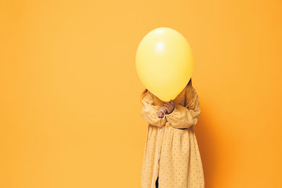 Top view of woman holding red balloon against yellow background