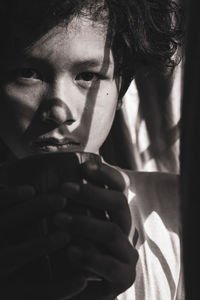 Close-up portrait of boy drinking coffee by window