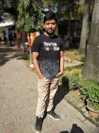 Full length portrait of young man standing on footpath during sunny day