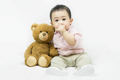 Portrait of cute baby boy with teddy bear against white background