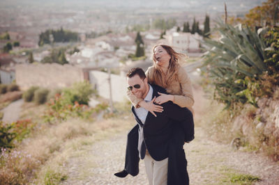 Man giving piggy back ride to happy woman standing on land