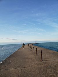 Rear view of man walking on pier by sea