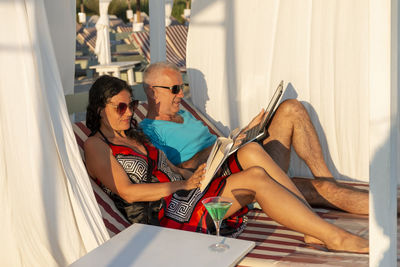 Married couple lying on a daybed. man is on his smartphone, while his wife working on her laptop.