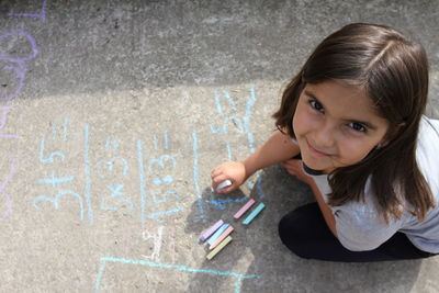 High angle portrait of girl writing with chalk on footpath