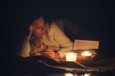 Young woman reading book while lying on bed with puppy