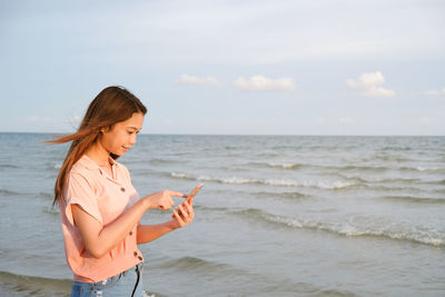 Young woman using mobile phone at beach against sky
