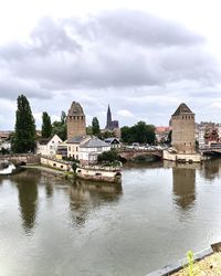 Buildings at waterfront against cloudy sky