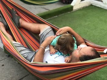 High angle view of father embracing baby while lying in hammock