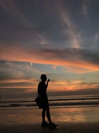 Silhouette man standing on beach against sky during sunset