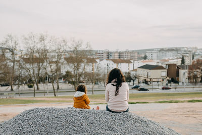 Rear view of women and daughter sitting on floor against sky