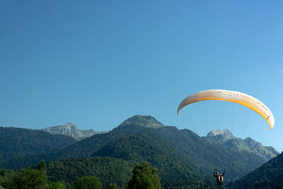 Man paragliding over mountains against clear sky