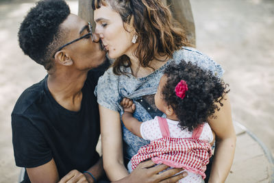 Baby girl looking at mother and father kissing in playground