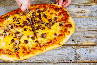 Cropped hands cutting pizza on wooden table