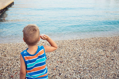 Rear view of boy standing on shore at beach