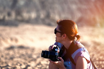 Side view of young woman photographing while standing on field