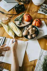 High angle view of different vegetables with food stylist writing in book at table