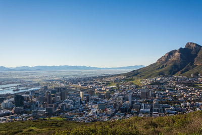 Aerial view of townscape by mountains against clear blue sky