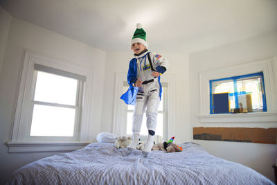 Happy boy wearing costume and jumping on bed at home