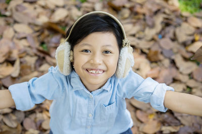 Portrait of happy girl with arms raised wearing ear muff in park