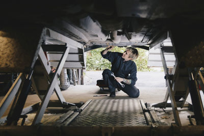 Female mechanic kneeling while examining under car at auto repair shop