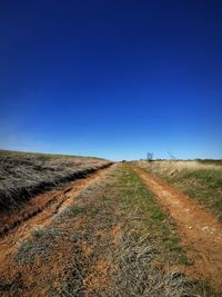 Dirt road along countryside landscape against clear blue sky