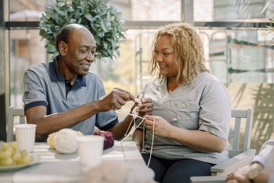 Smiling female nurse assisting senior man in crocheting at nursing home