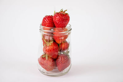 Close-up of strawberries in glass jar against white background