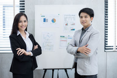 Portrait of colleagues with arms crossed standing by whiteboard in office